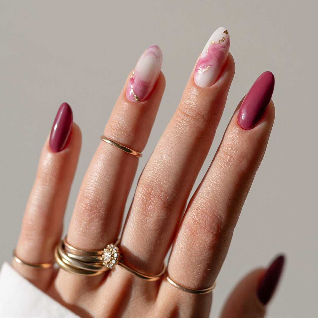 Manicure rosa e bordeaux con dettagli dorati e anelli.