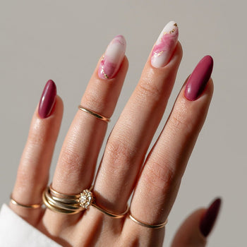 Manicure rosa e bordeaux con dettagli dorati e anelli.